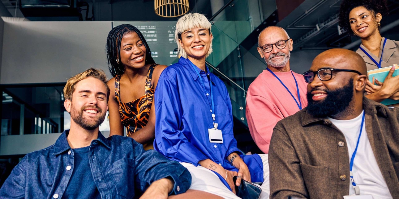 Six men and woman of different ages and ethnicities sit together mostly looking at the camera